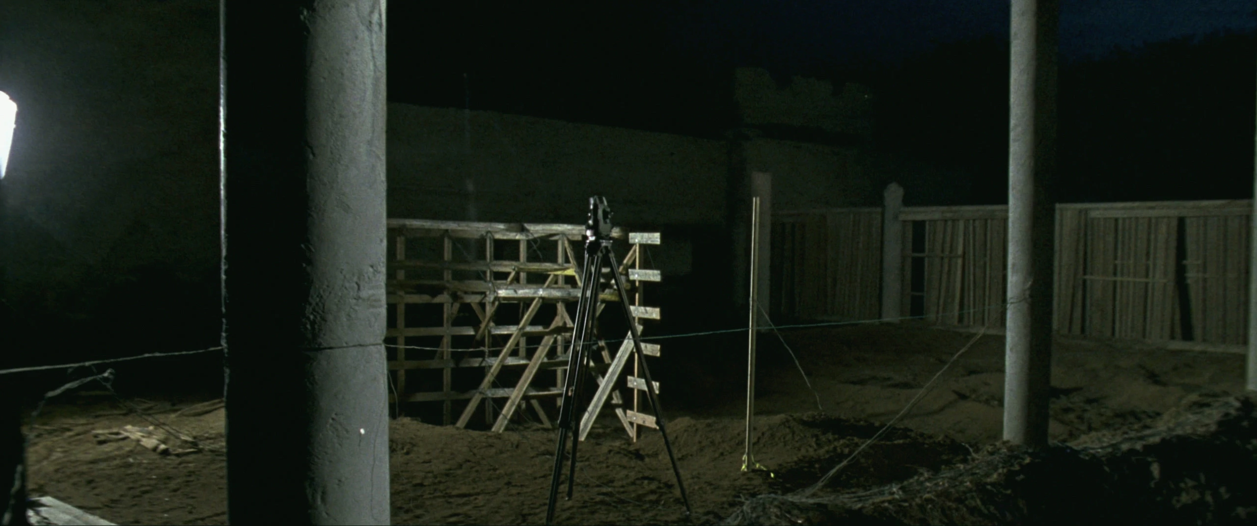 A surveyor's instrument on a tripod among string lines and timber formwork at night
